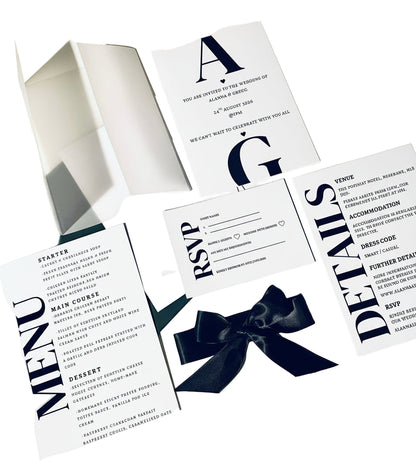 Wedding invitation set with black bow, menu, and RSVP card on a white background